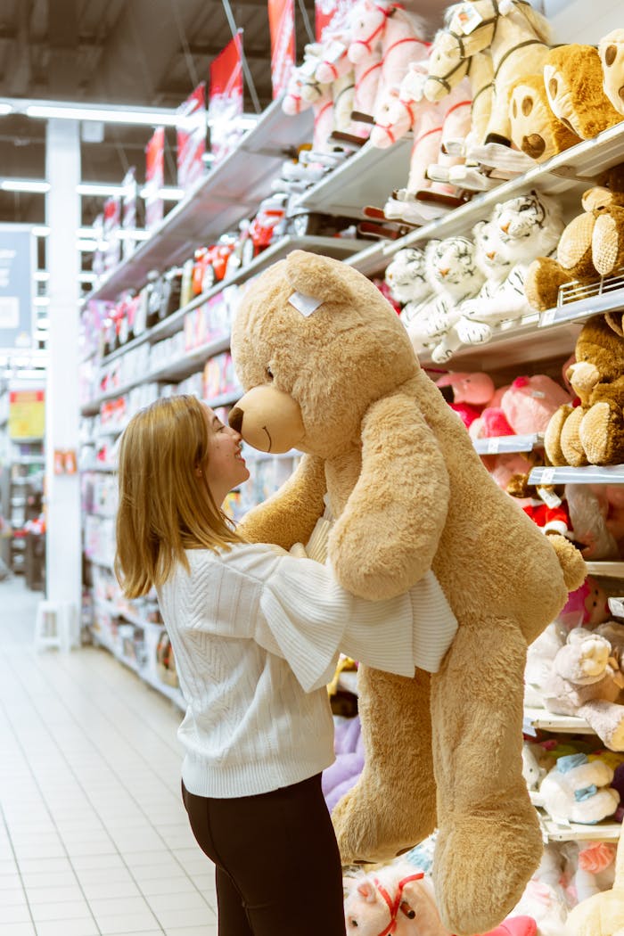 A woman chooses a large teddy bear in a retail toy section, surrounded by stuffed animals.