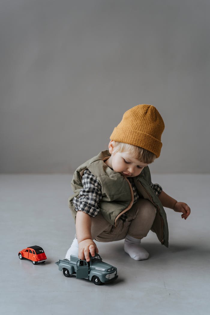Cute toddler in stylish attire playing with toy trucks on the floor, captured indoors.